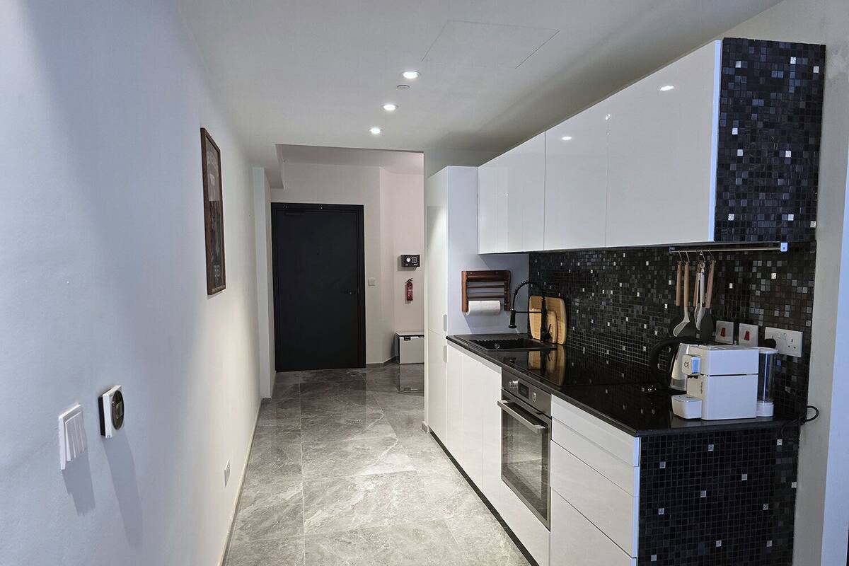 Une cuisine moderne avec des meubles blancs, un pare-feu noir et un sol carrelé.