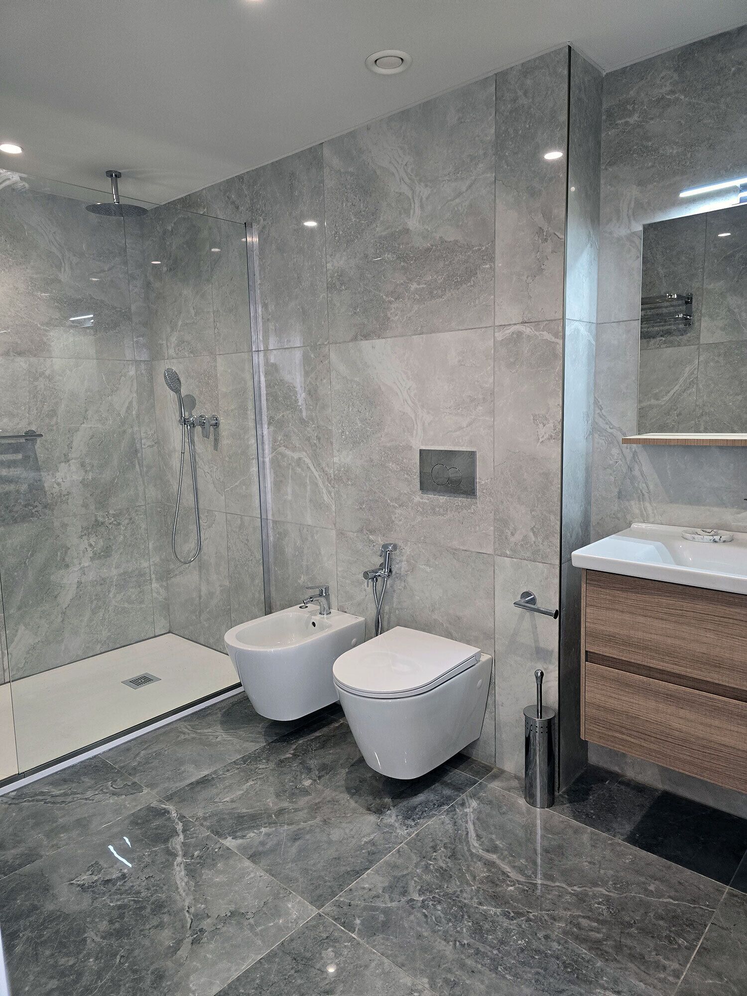 Un baño moderno con ducha a ras de suelo, dos bidés, un lavabo y un espejo.