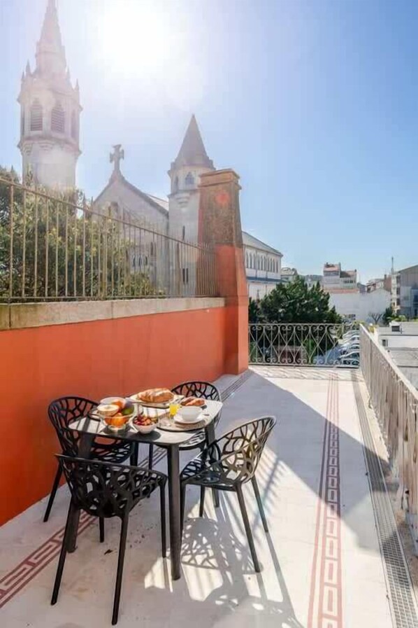 Un balcón con una mesa preparada para una comida, sillas y vistas a una iglesia con dos torres.