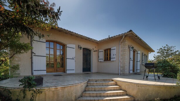 A two-story house with a stone facade, a front porch with steps, and a barbecue grill.