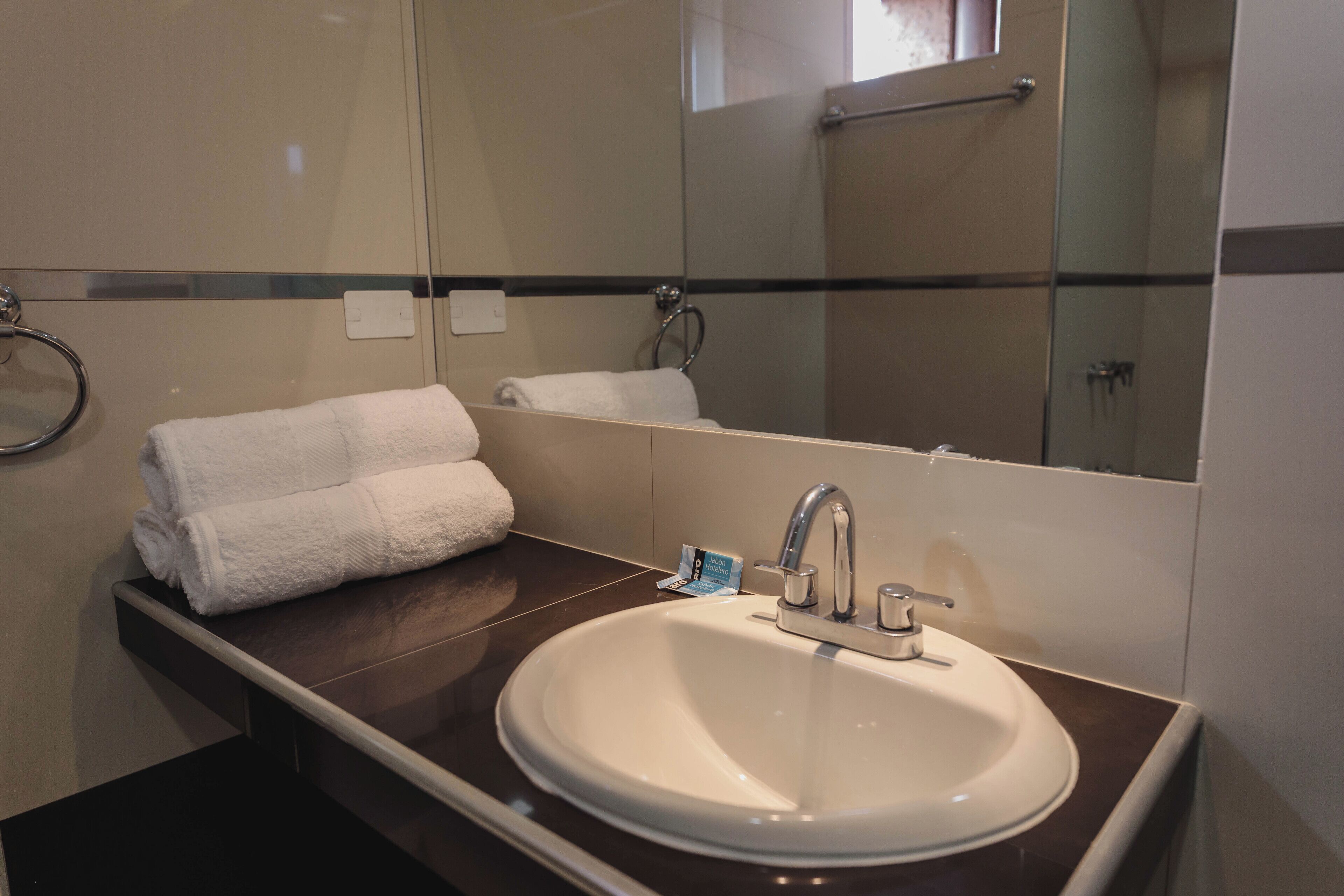 A bathroom with a white sink, a mirror, and two towels on a dark countertop.