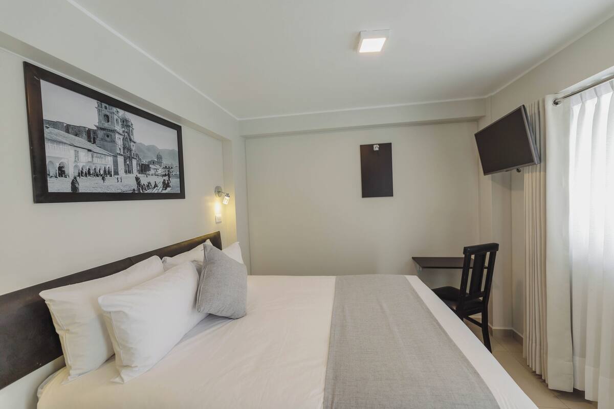 Ein Hotelzimmer mit einem großen Bett, einem Schreibtisch, einem Sessel, einem Fernseher und einem gerahmten Bild an der Wand.