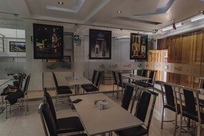 Un restaurante moderno con paredes de vidrio, sillas negras y mesas. Hay carteles en las paredes y un letrero que indica la salida.