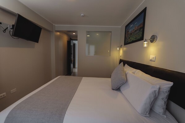 Een hotelkamer met een bed, een wandtelevisie, een schilderij en een wandlamp.