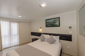 Een hotelkamer met een groot bed, een nachtkastje, een wandlamp en een raam met gordijnen.