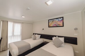 Una habitación de hotel con dos camas, un cuadro en la pared y una ventana con cortinas.