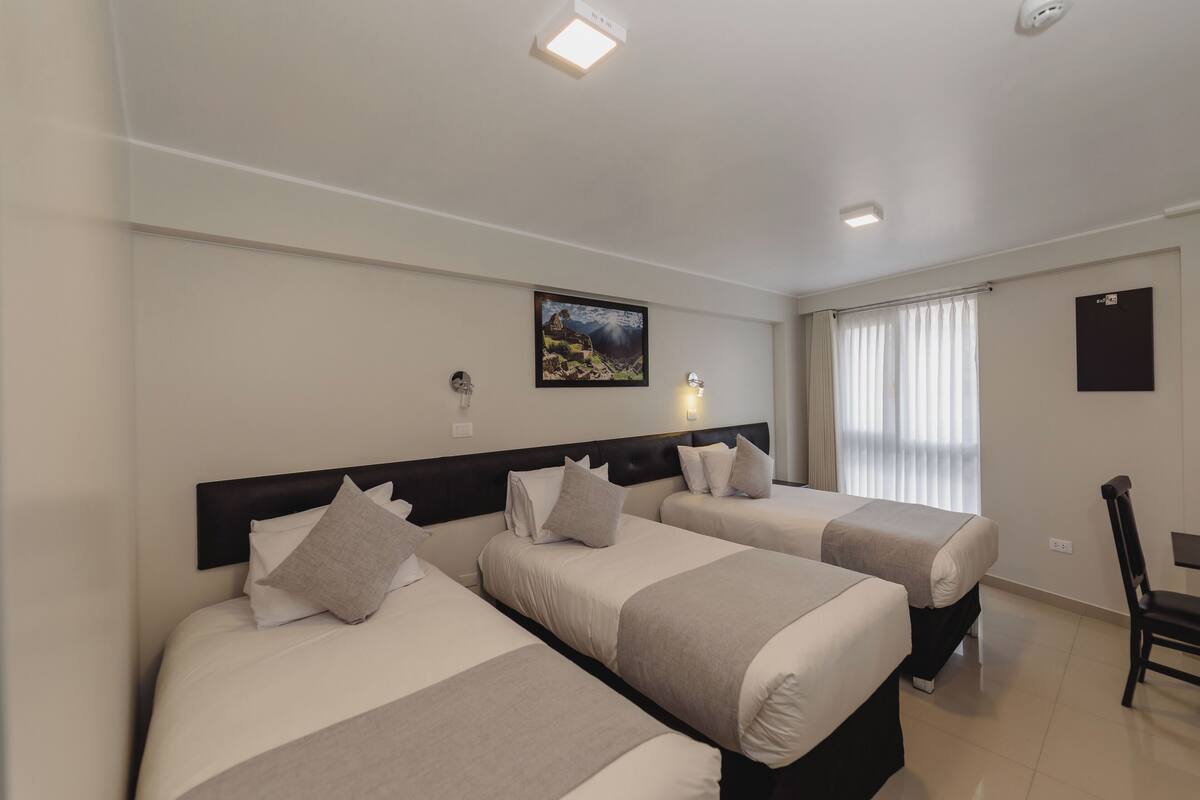 Ein Hotelzimmer mit zwei Betten, einem Schreibtisch, einem Sessel, einem Bild an der Wand und einem Fenster mit Vorhängen.