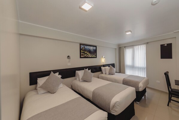 Habitación de hotel con dos camas, un escritorio, una silla, un cuadro en la pared y una ventana con cortinas.