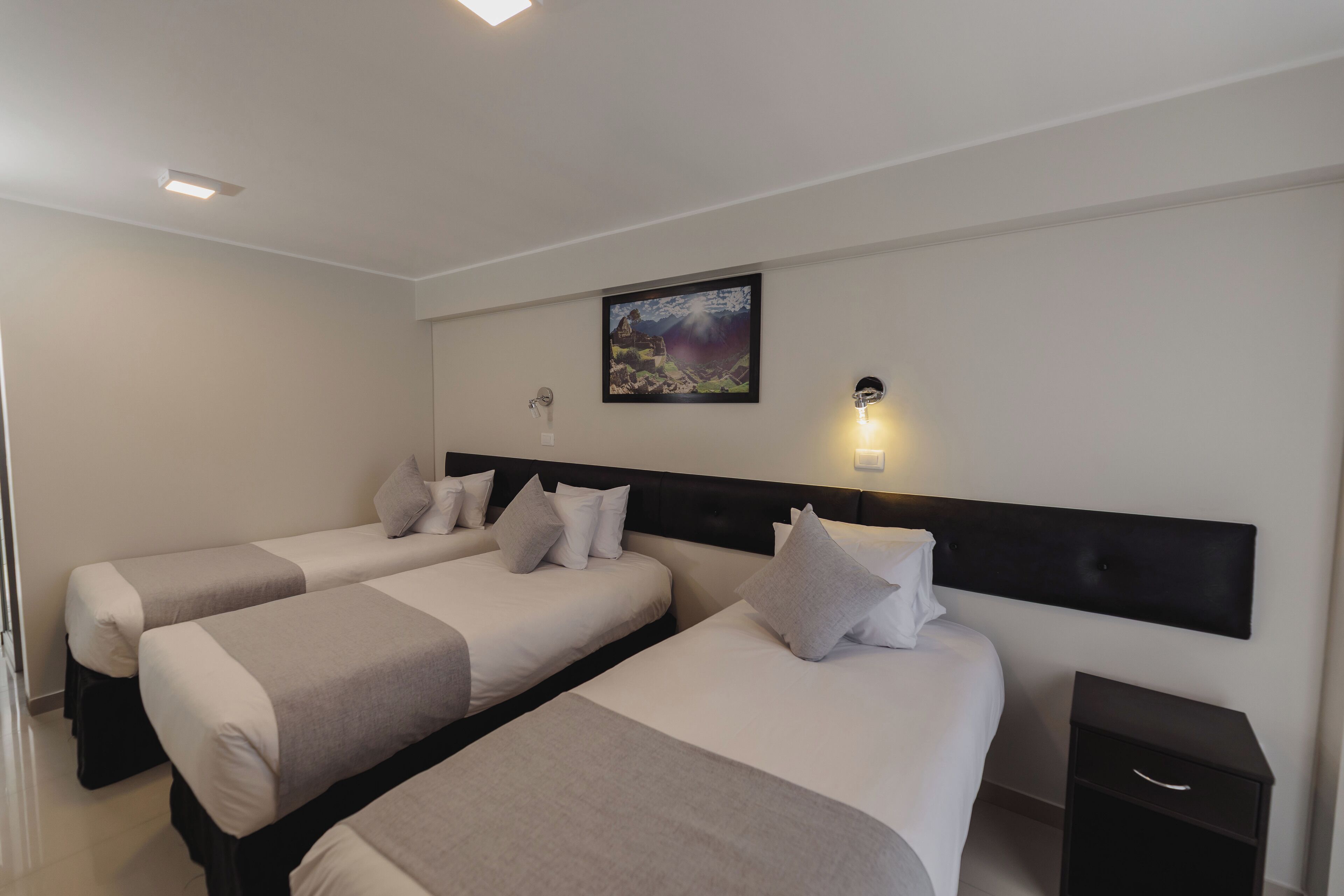 Une chambre d’hôtel avec deux lits, une table de chevet, une lampe fixée au mur et un tableau encadré.