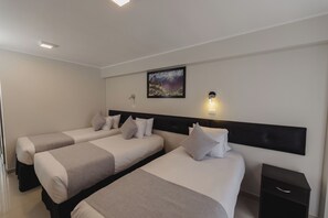 Habitación de hotel con dos camas, una mesita de noche, una lámpara fijada a la pared y un cuadro enmarcado.