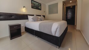 Un dormitorio moderno con una cama grande, una mesita de noche, una lámpara de pared y una puerta que da a otra habitación.