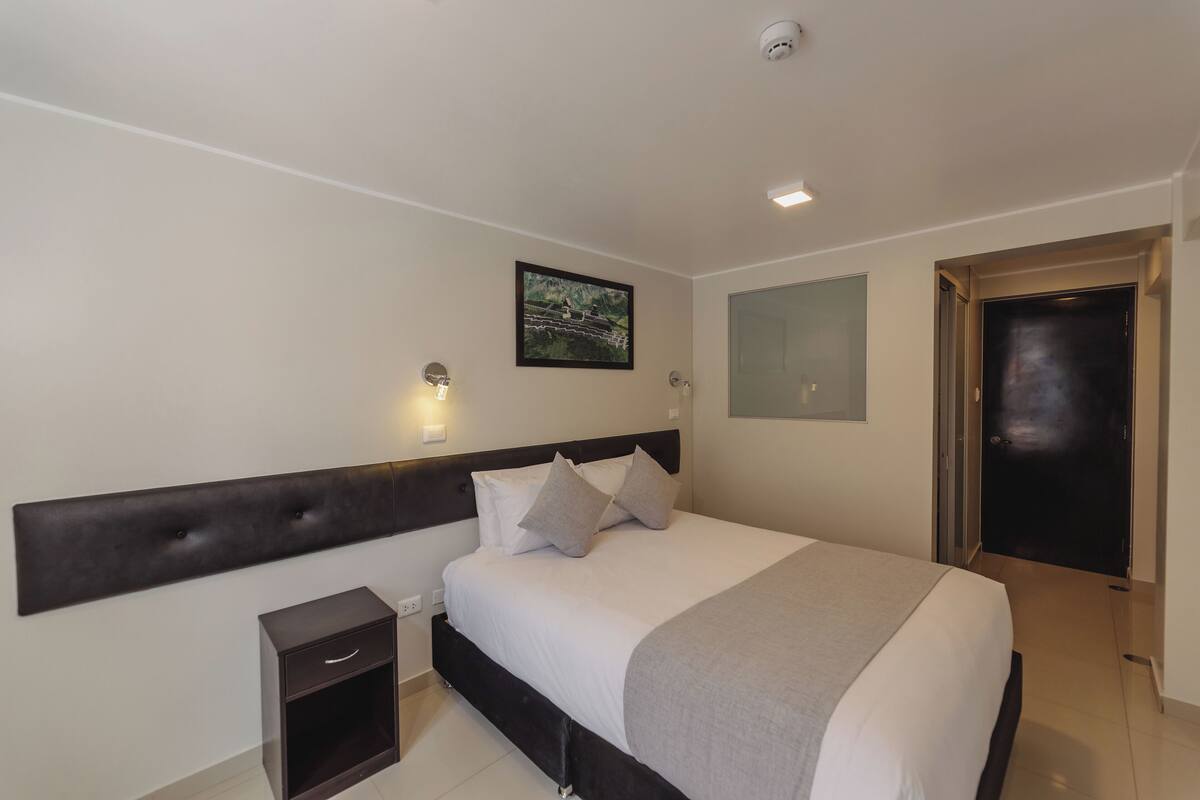 Ein modernes Hotelzimmer mit einem großen Bett, einem Nachttisch, einer Wandleuchte und einer Tür.