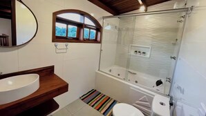 Une salle de bain avec un meuble-lavabo en bois, un grand miroir, une douche avec une paroi en verre et une petite fenêtre.
