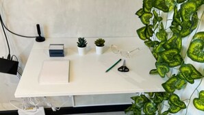 Un bureau blanc avec une chaise noire, une petite plante en pot, une paire de lunettes et un crayon.