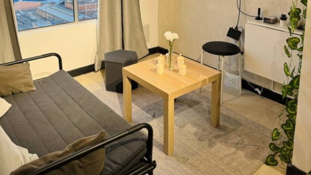 Une chambre moderne avec un lit, une petite table avec des bougies, une télévision et une vue sur le paysage urbain à travers de grandes fenêtres.