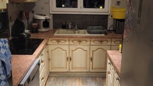 A kitchen with wooden cabinets, a stainless steel refrigerator, a window with a view of the sunset, and a sink. - Private room (Allonnes)