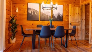 Un interior de madera con una mesa de comedor, sillas, una araña y dos cuadros en la pared.