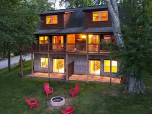 Una cabaña de madera de dos pisos con balcón, varias ventanas y un hogar en el jardín.
