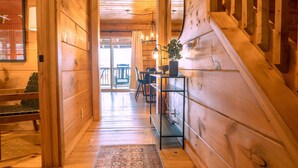 A wooden interior with a staircase, a dining area, and a view to the outside. - 11BR Retreat | 2 Cabins | Walk to WJ | Sleeps 27 (West Jefferson)