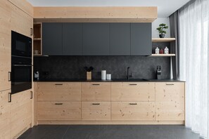 Een moderne keuken met houten kastjes, een zwart aanrecht en een donkere achterwand.