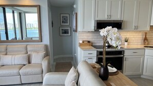 A modern living room with a white sofa, a wooden coffee table, and a kitchen area with white cabinets and a microwave.