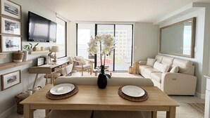 A modern living room with a dining area, a flat-screen TV, and a balcony with a city view.