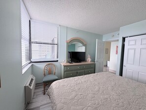 A bedroom with a bed, a dresser, a chair, a television, and a window with blinds.