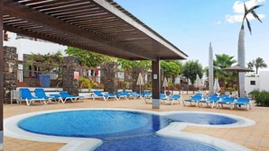A pool area with two circular pools, lounge chairs, and a covered seating area. - Playa Flamingo Bellavista (Playa Blanca)