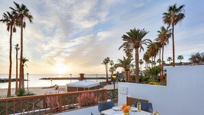A terrace with a table set for two, overlooking a beach with palm trees and a sunset. - Playa Flamingo Bellavista (Playa Blanca)