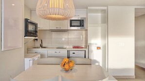 A modern kitchen with white cabinetry, a built-in microwave, and a dishwasher. A fruit bowl is on the dining table. - Playa Flamingo Bellavista (Playa Blanca)