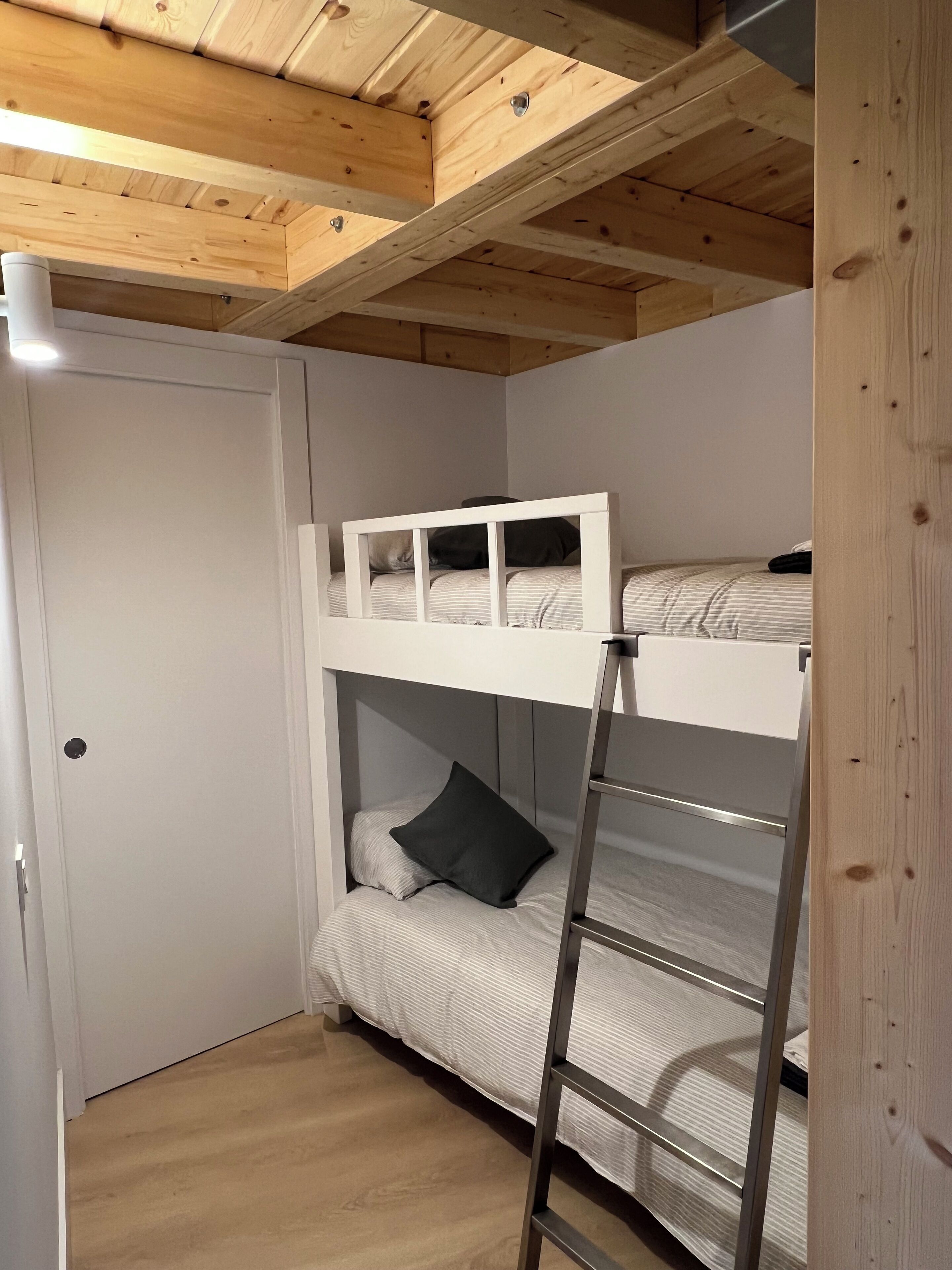 A bunk bed room with a ladder, wooden ceiling beams, and a door.