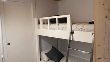 A bunk bed room with a ladder, wooden ceiling beams, and a door.