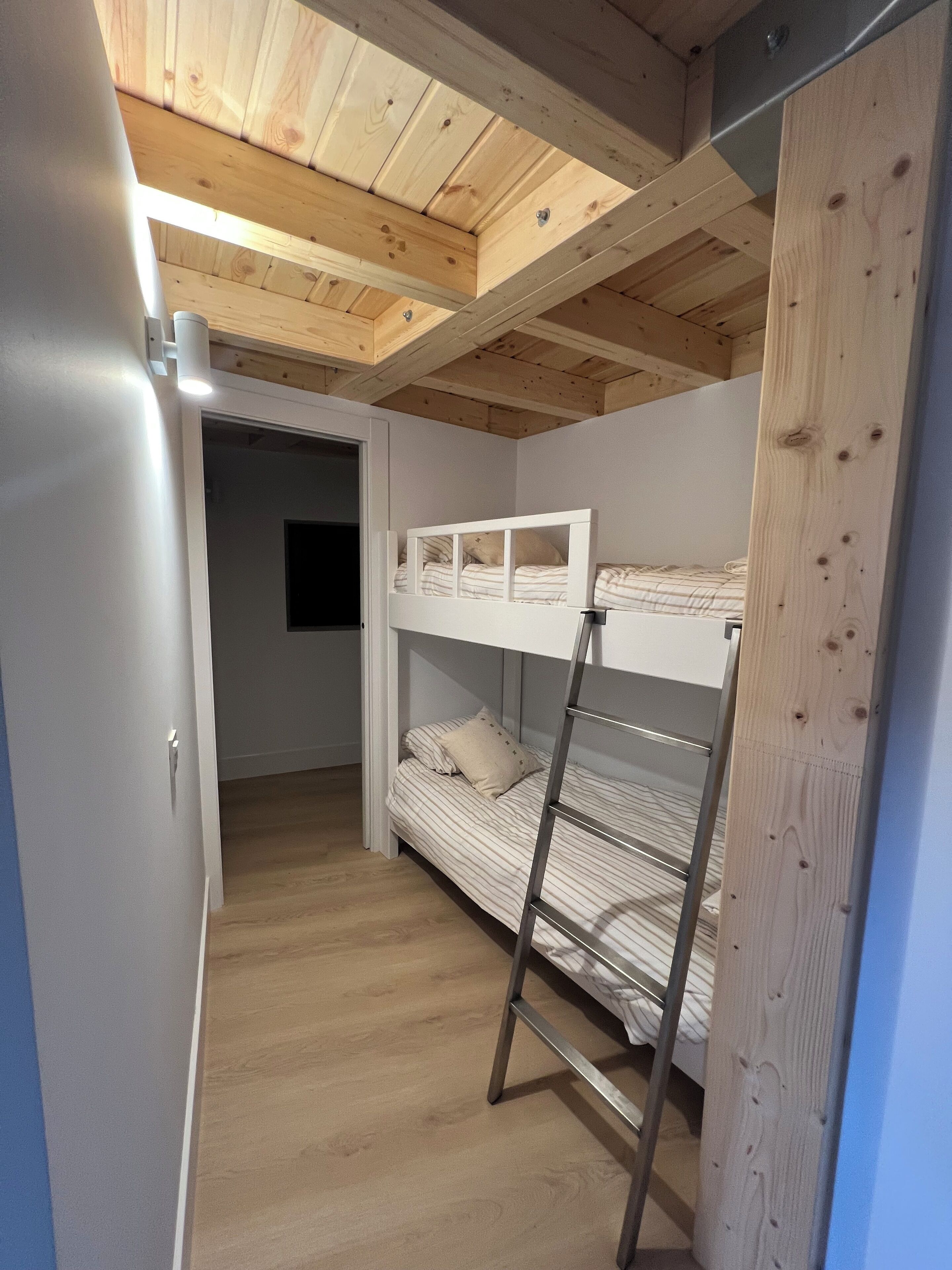 A bunk bed room with a wooden ceiling and a ladder.
