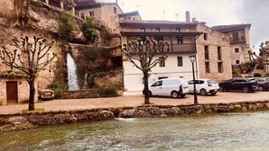 A stone building with a waterfall, parked cars, and a river. - La Tahona Cántabra (Orbaneja del Castillo)