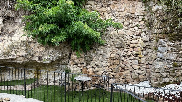 A stone wall with a garden area, including a metal fence, a small table, and chairs. - La Tahona Cántabra (Orbaneja del Castillo)