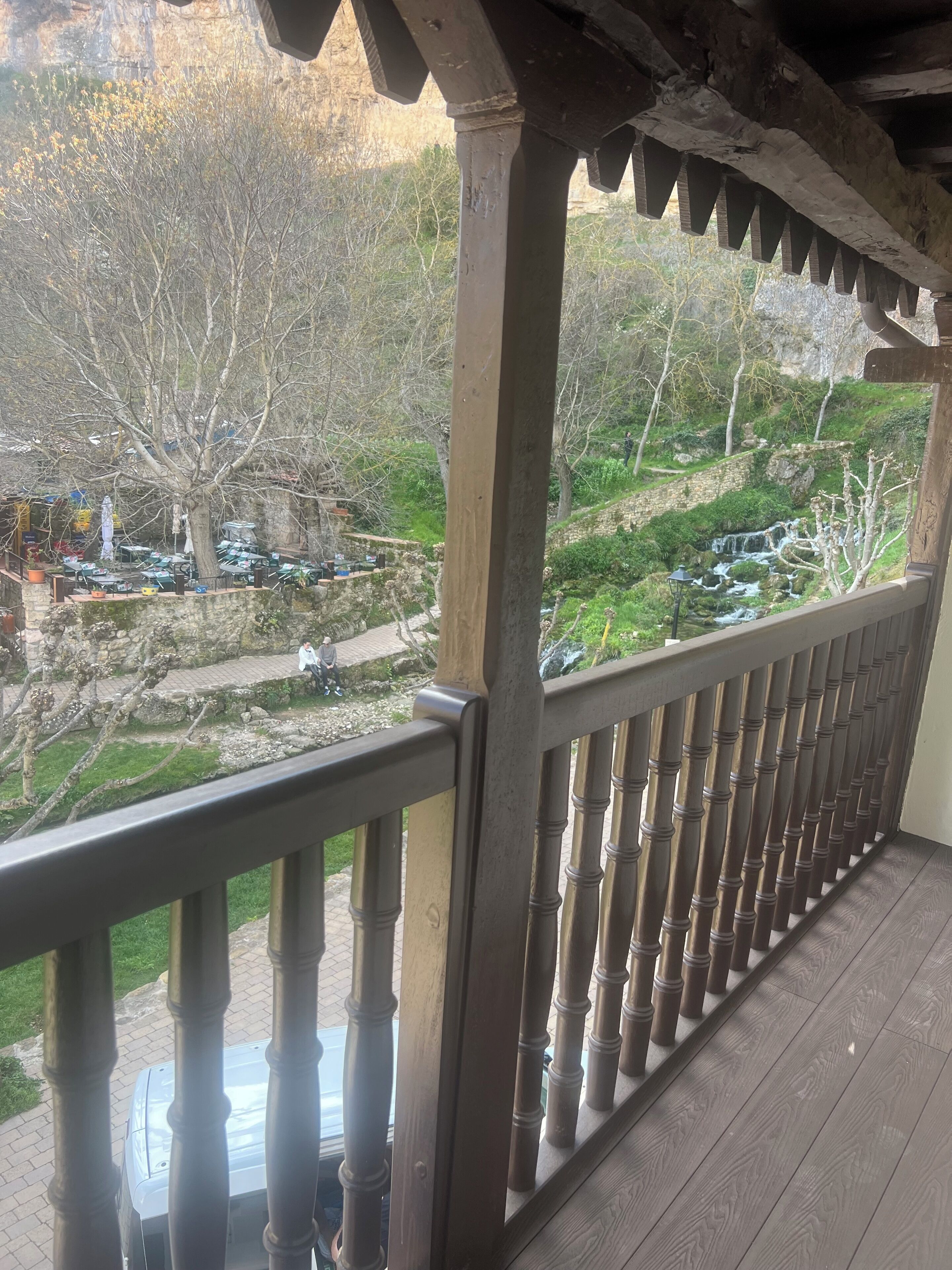 A wooden balcony with a view of a rocky hillside and a small waterfall.