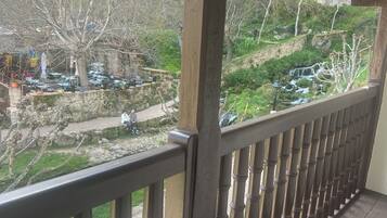 A wooden balcony with a view of a rocky hillside and a small waterfall.