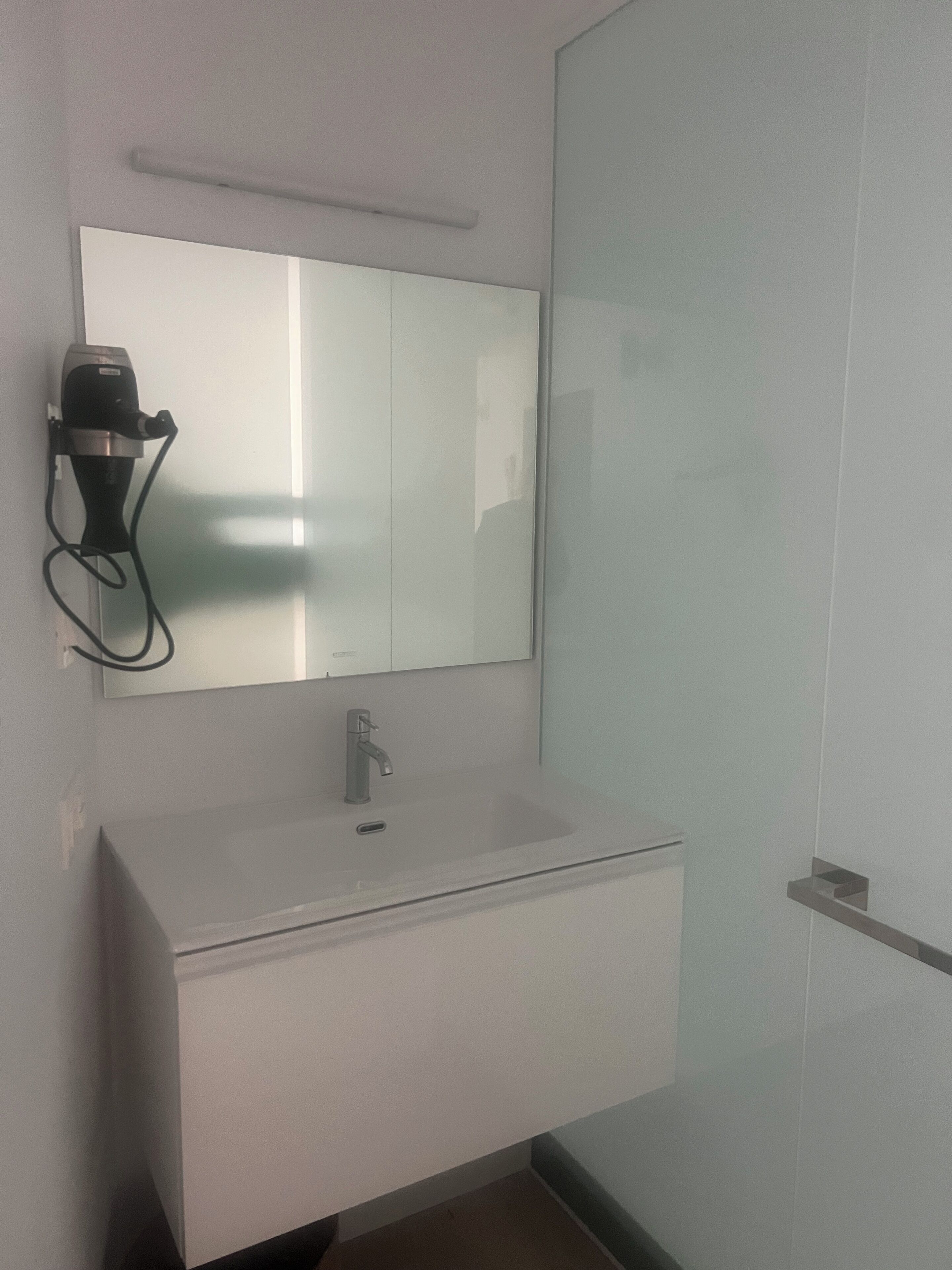 A modern bathroom with a white sink, a mirror, and a hairdryer mounted on the wall.