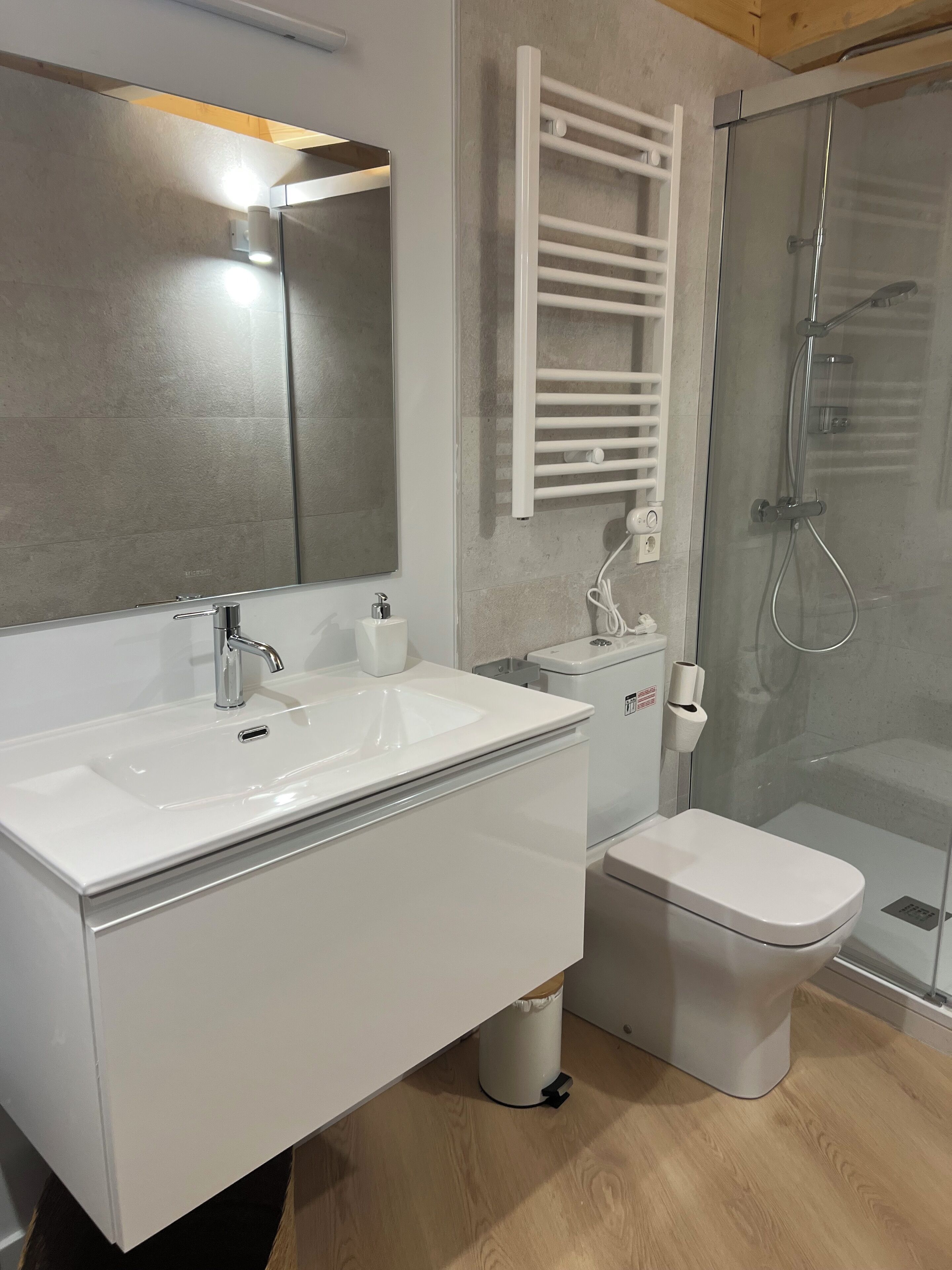 A modern bathroom with a white sink, mirror, and toilet. There is a glass shower enclosure with a glass door.