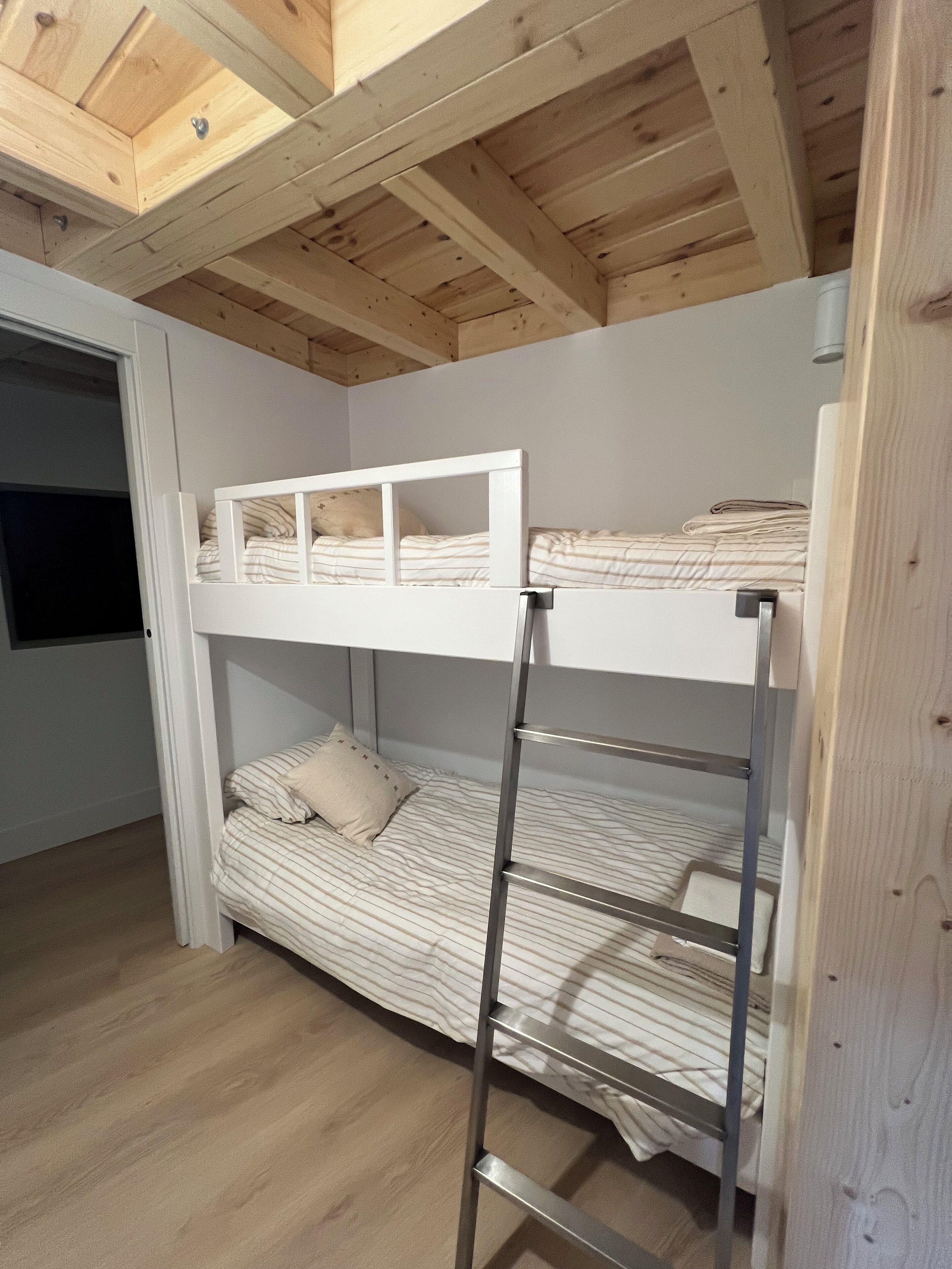 Een slaapkamer met een stapelbed, houten plafond en een metalen ladder.