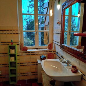 Enjoy a serene bathroom retreat with a view of the surrounding woods, featuring a sink, mirror, and storage shelf.