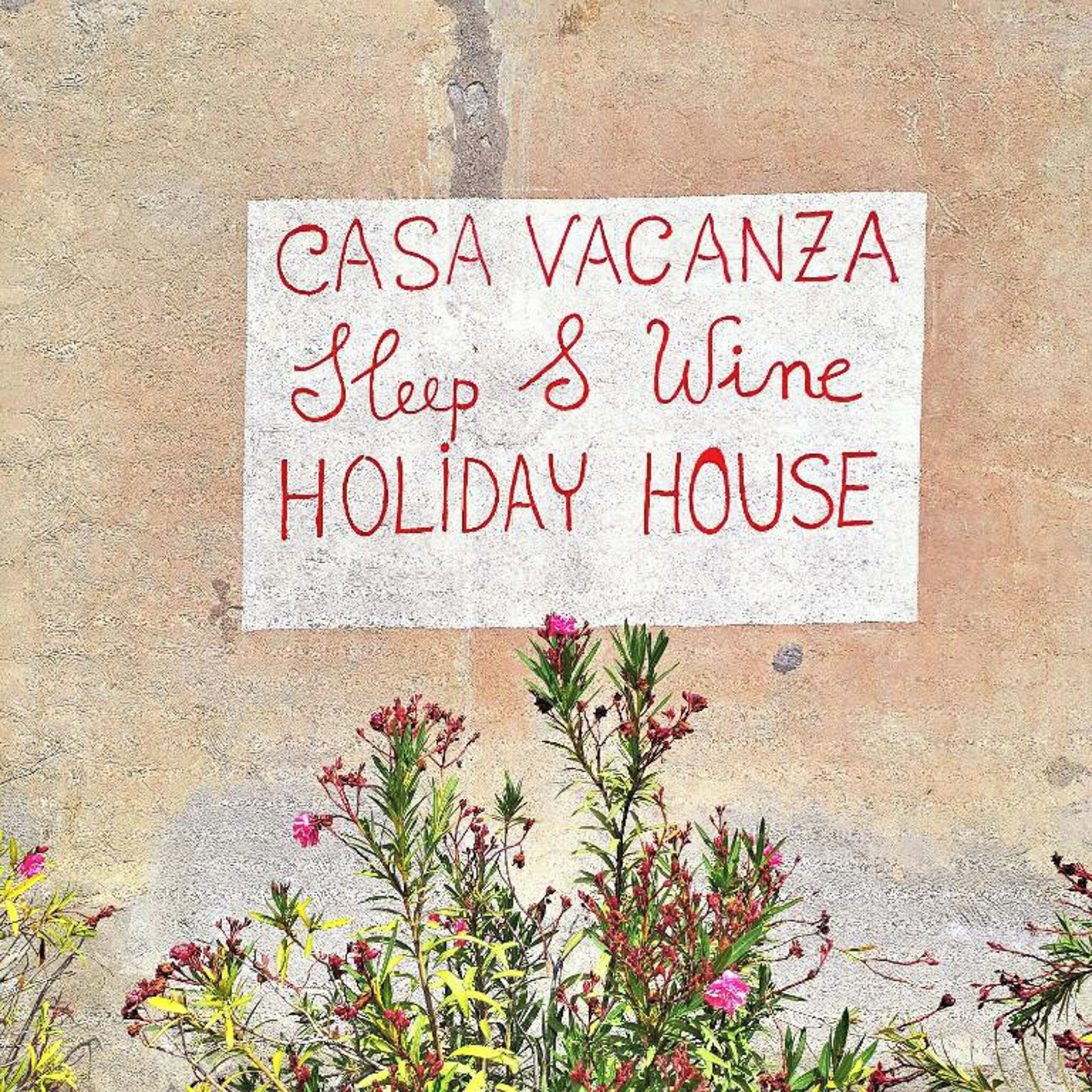 A sign advertising a 'CASA VACANZA Sleep & Wine HOLIDAY HOUSE'.