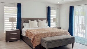 A bedroom with a bed, bedside tables, a ceiling fan, and large windows with curtains. - 664 Naples Beach Paradise-Your Next Vacation Spot with Private Pool & Spa (Naples)