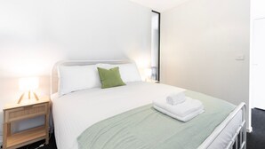 A neatly made bed with white and green bedding, a bedside lamp, and a folded towel on the bed.