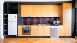 A compact kitchen with wooden cabinets, a stainless steel refrigerator, an oven, a microwave, and a dishwasher.