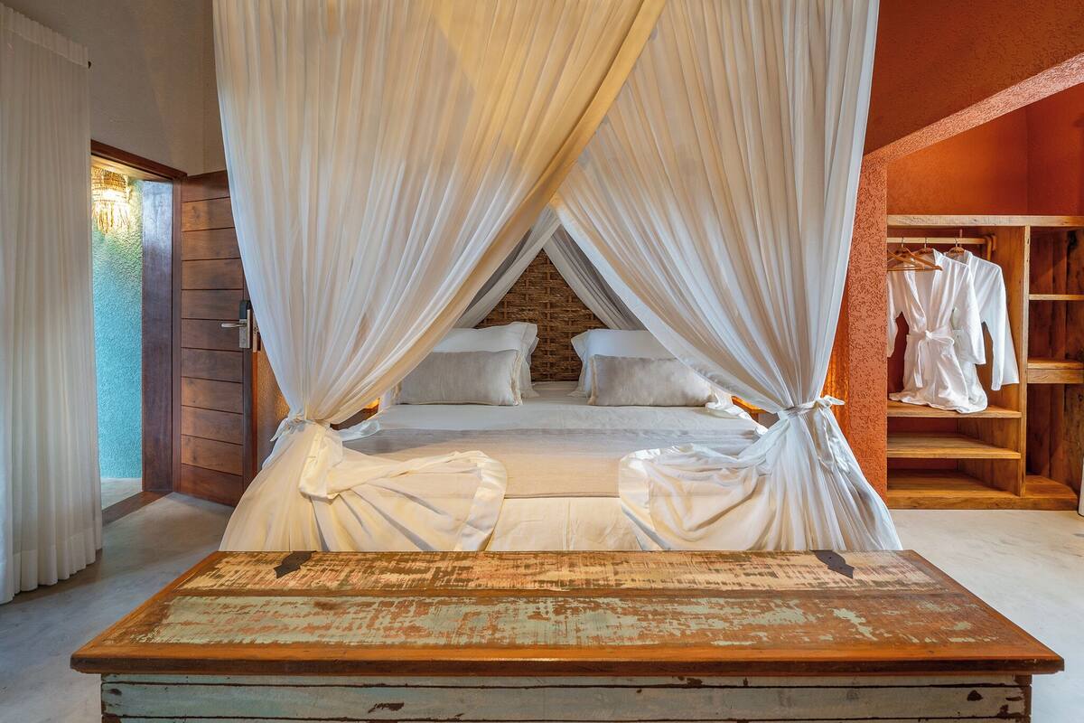 A bed with a canopy, a wooden bench, and a wooden wardrobe.