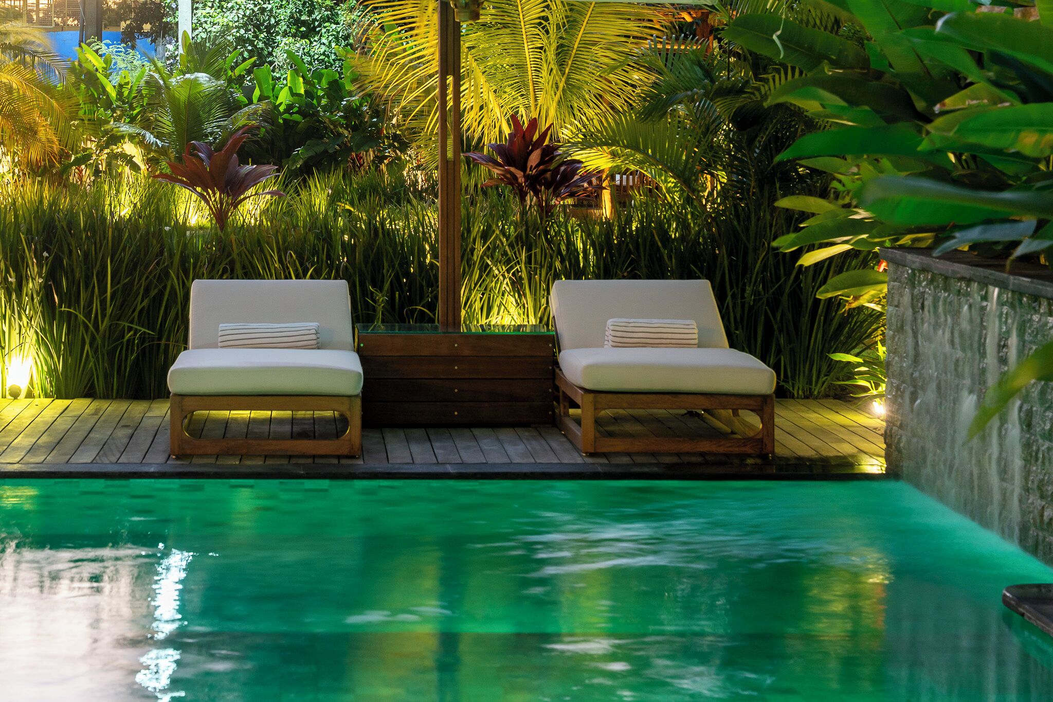Área da piscina com duas espreguiçadeiras e um deck de madeira.