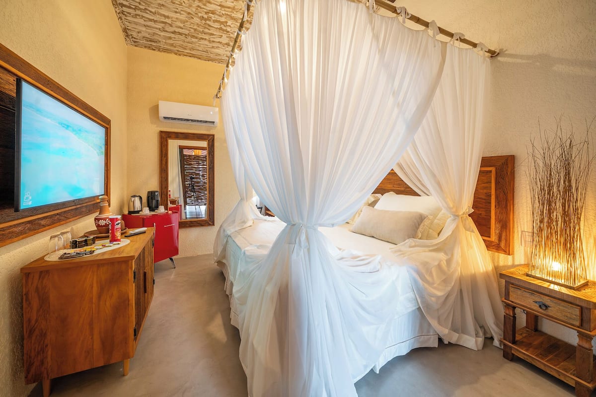 A bedroom with a canopy bed, a TV, a desk with a red chair, and a wooden nightstand.