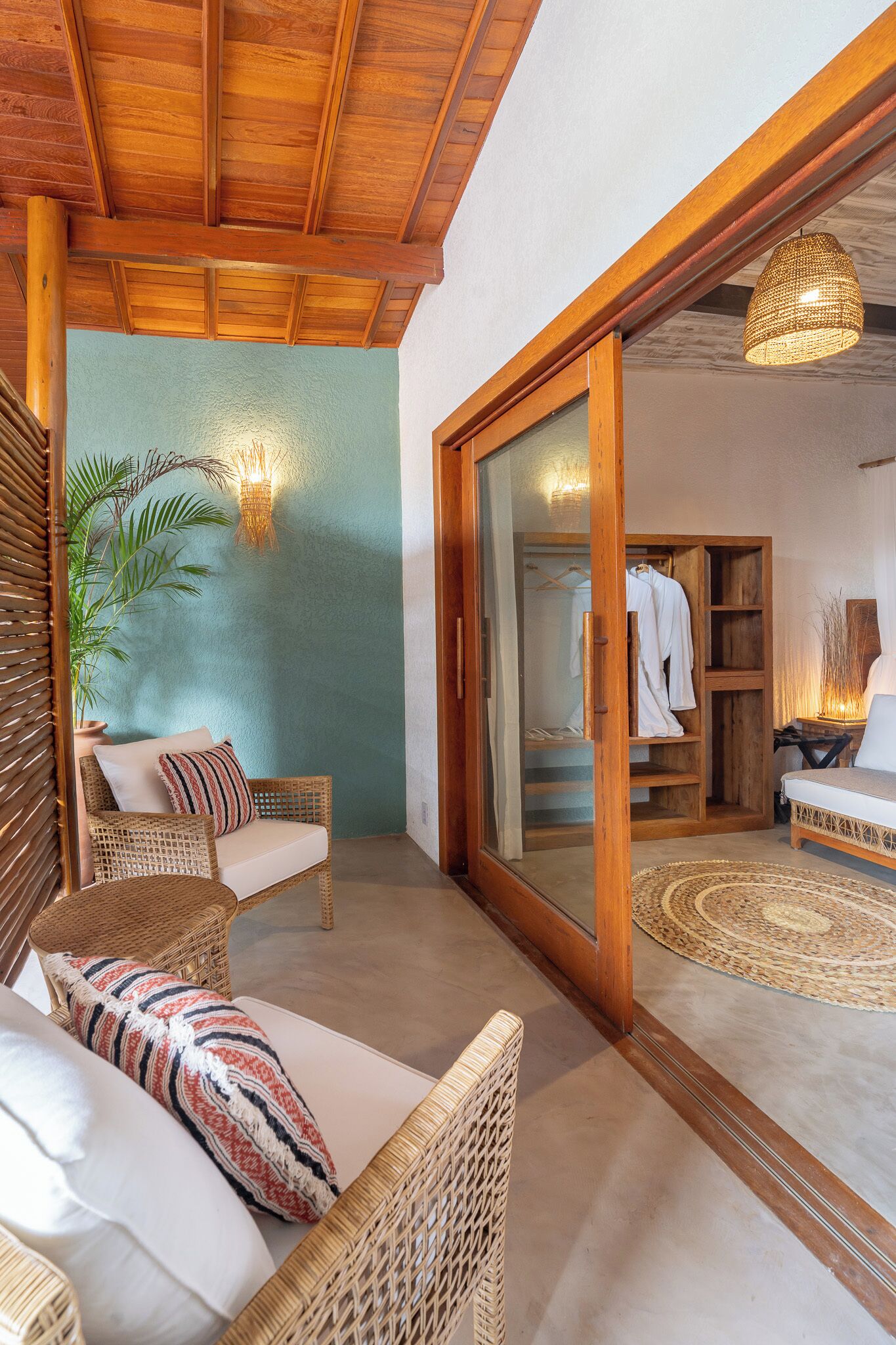Una habitación con muebles de mimbre, un ventanal corredero que da al baño y un techo con vigas de madera.