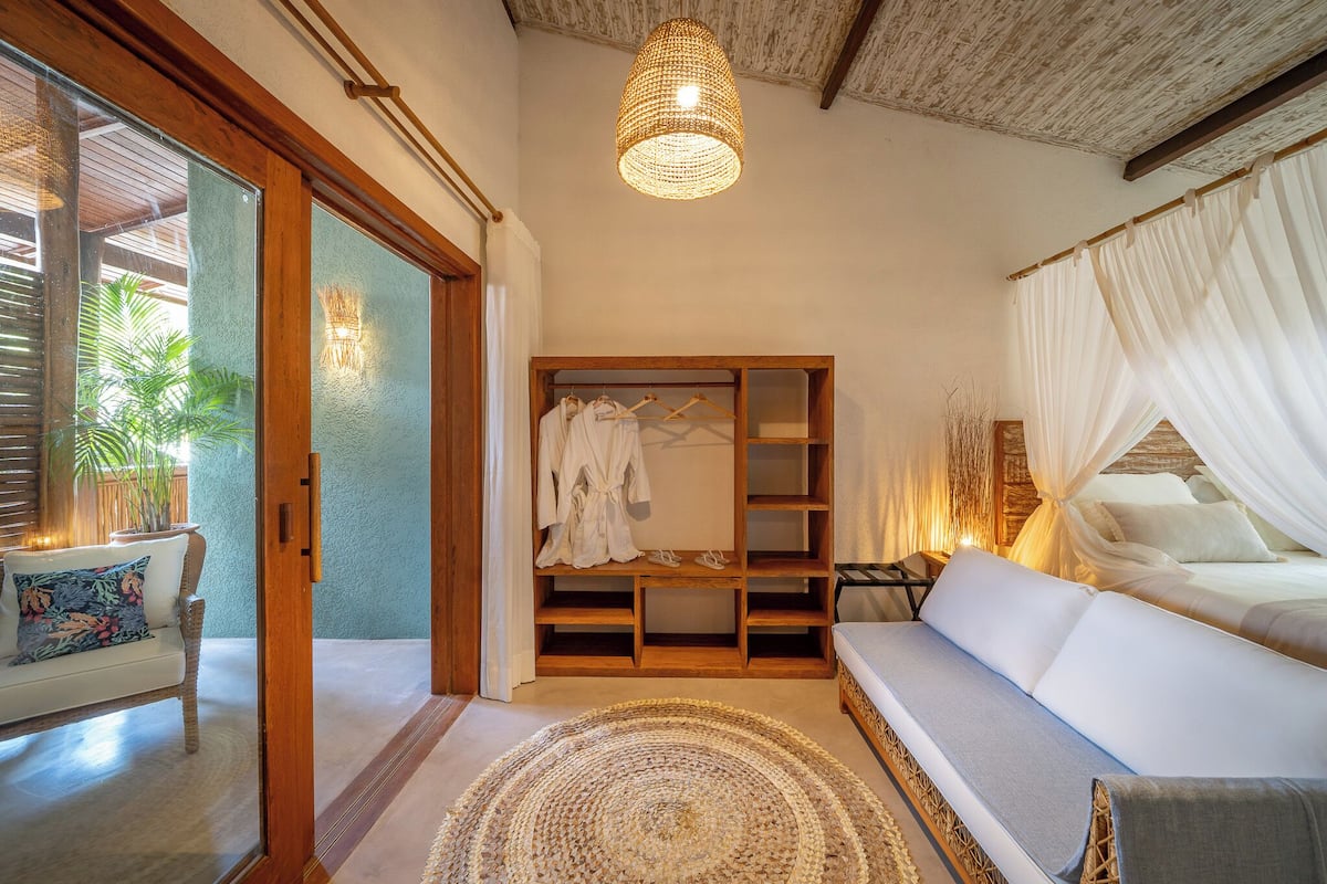 A room with a wooden bench, a white sofa, a hanging light fixture, and a wooden wardrobe.